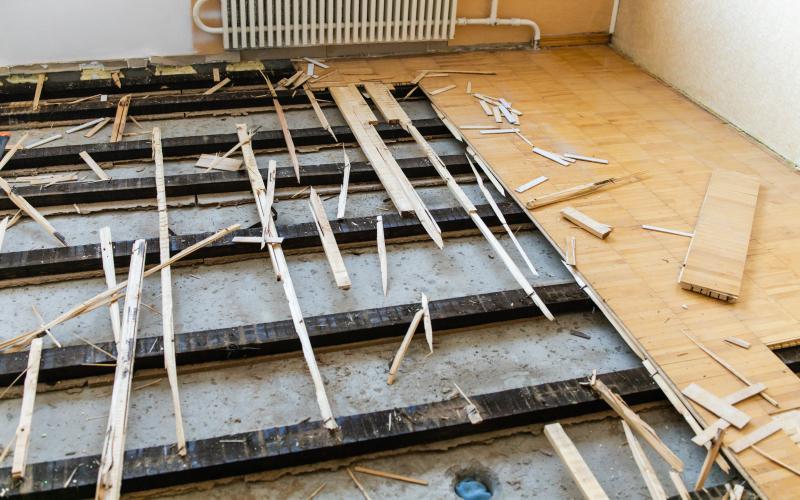 Teilweise entfernte Holzdielen geben den Blick auf den Unterboden und verstreuten Schutt in einem Raum mit einem Heizkörper frei. HDO GmbH - Ihr Handwerksdienstleister Oberschwaben - Jahnstraße 46 | 88214 Ravensburg